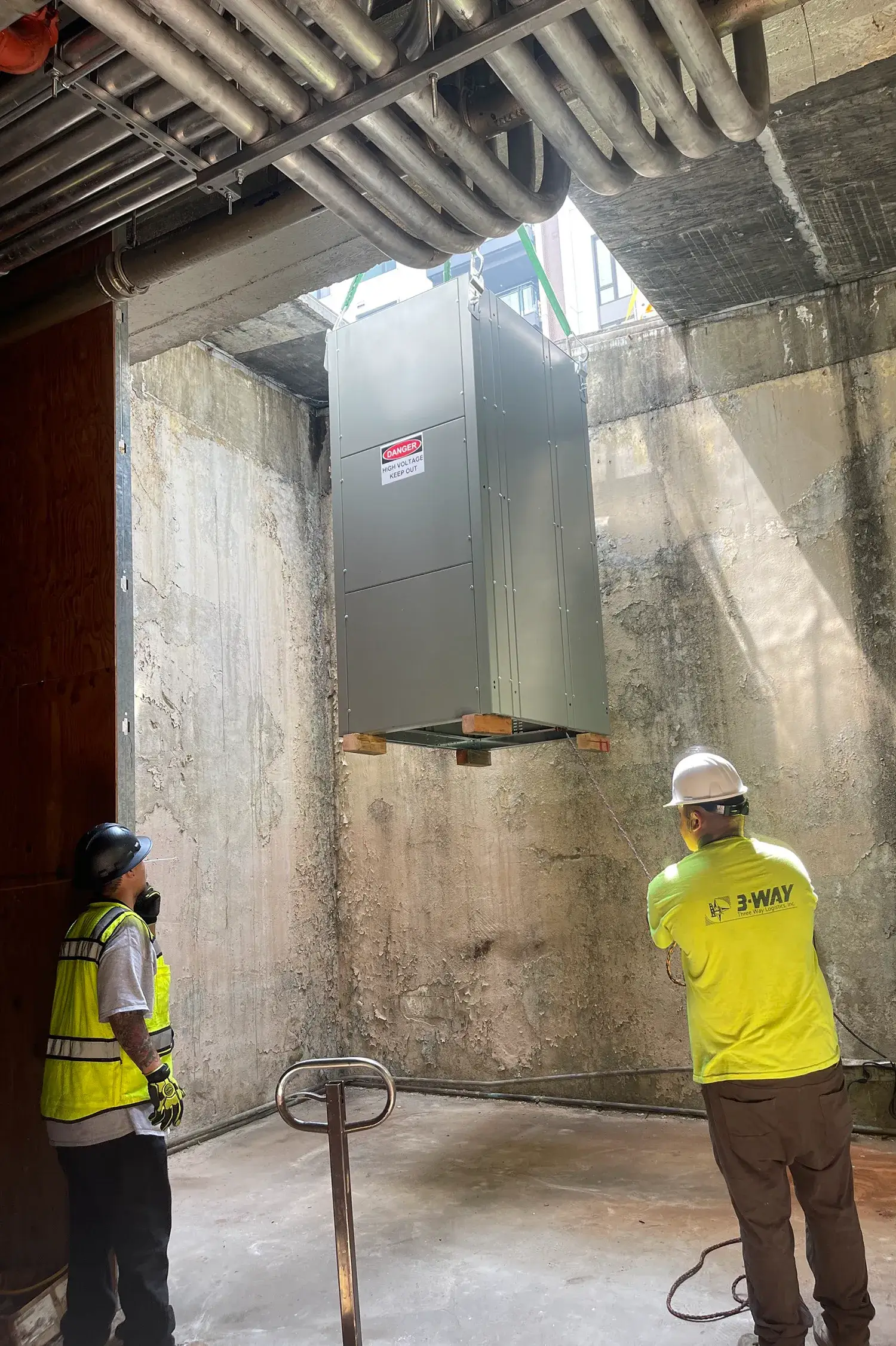 Two Three Way Logistics machinery movers rigging a large piece of equipment into the air