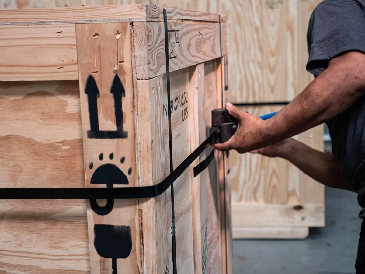 A logistics worker securing a crate with a strap
