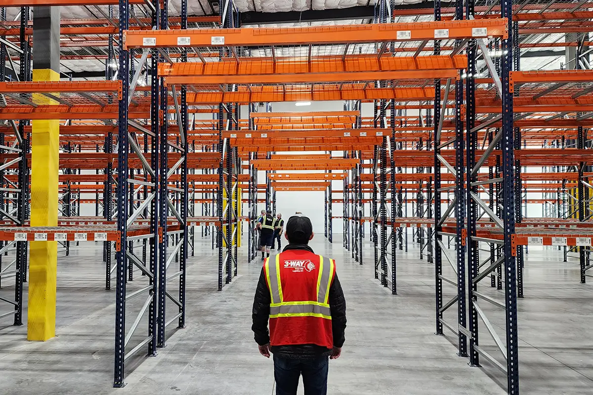 Three Way Logistics team member standing in a large warehouse aisle with empty storage racks, overseeing organized distribution and storage operations.